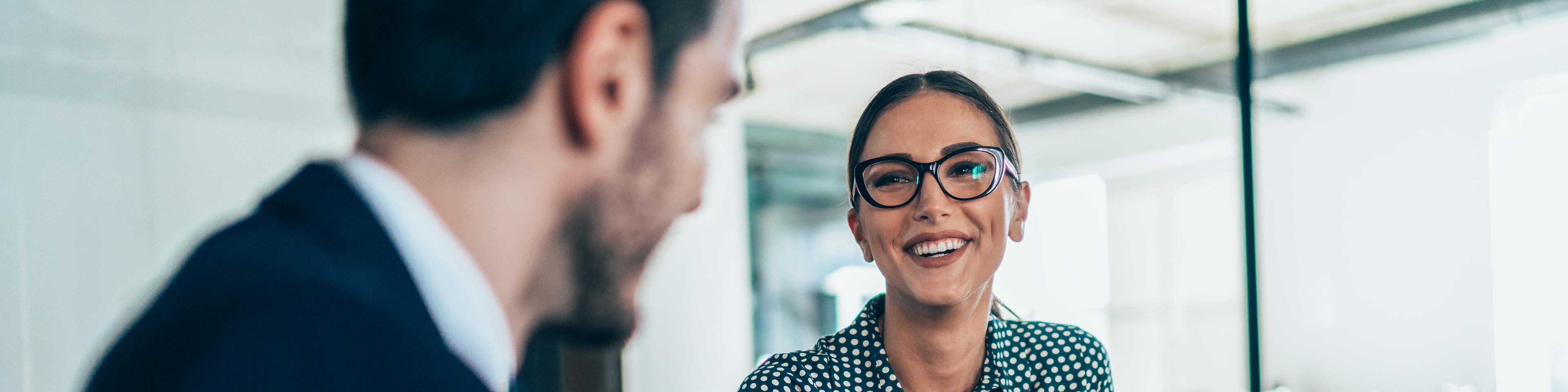 A woman with glasses holding a pen and smiling with her colleague