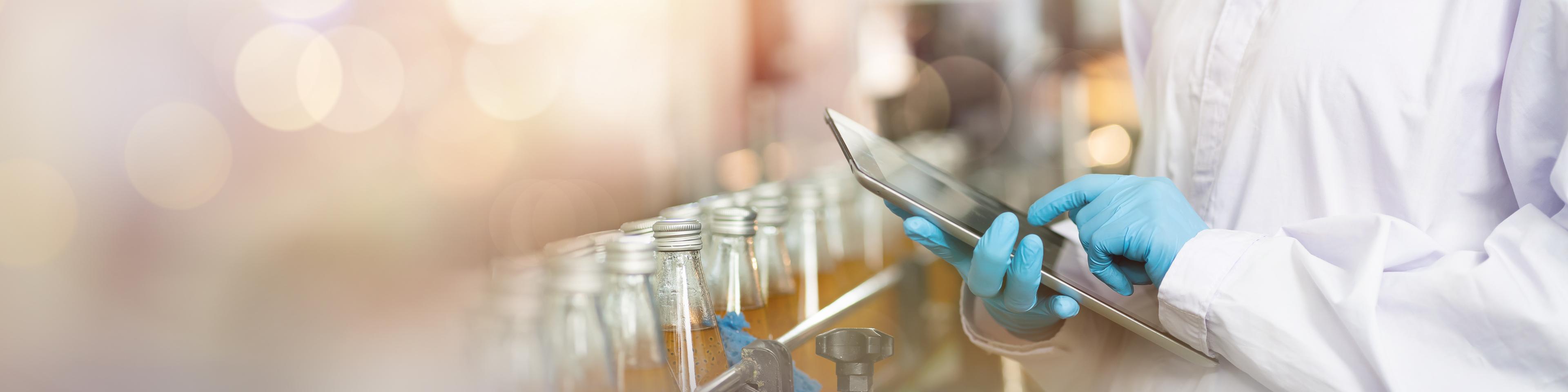 Hands of worker working with digital tablet check product on the conveyor belt in the beverage factory. Worker checking bottling line for processing. Inspection quality control