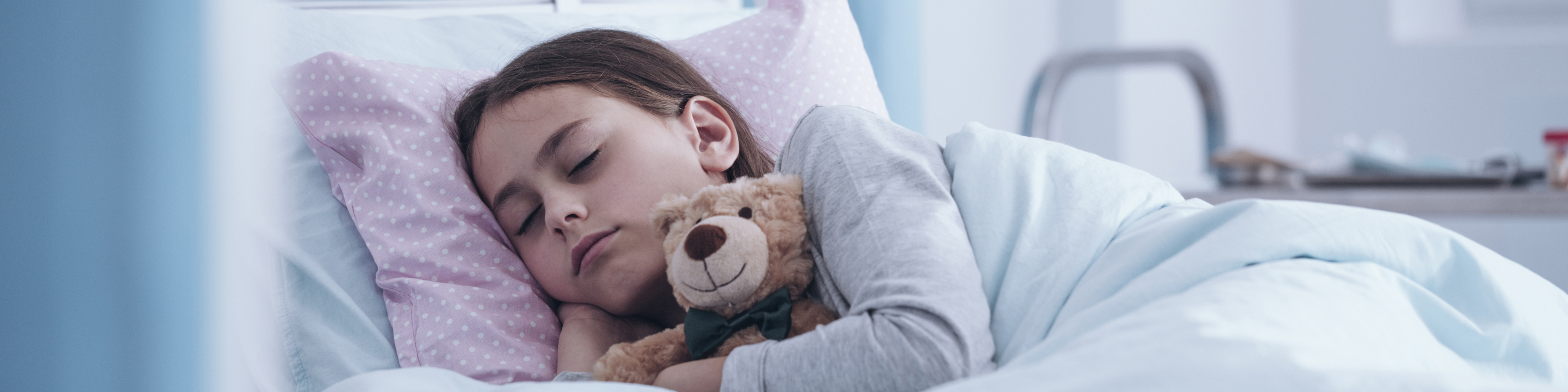 Child snuggling teddy bear while sleeping in hospital bed
