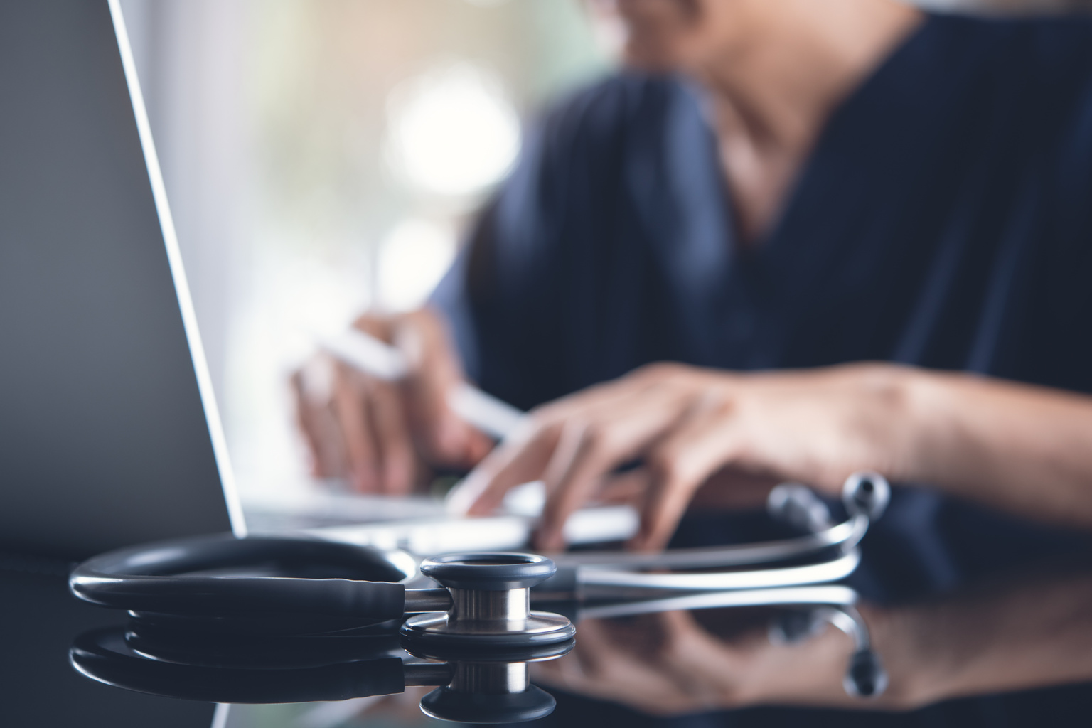 Doctor working on laptop computer with stethoscope in focus in foreground