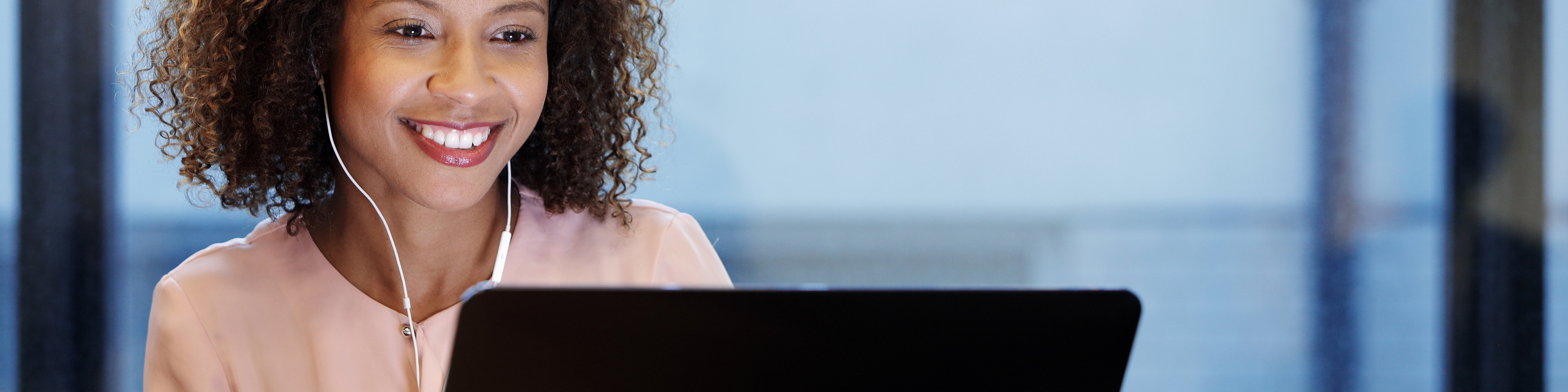 Young smiling businesswoman wearing earphones, using laptop