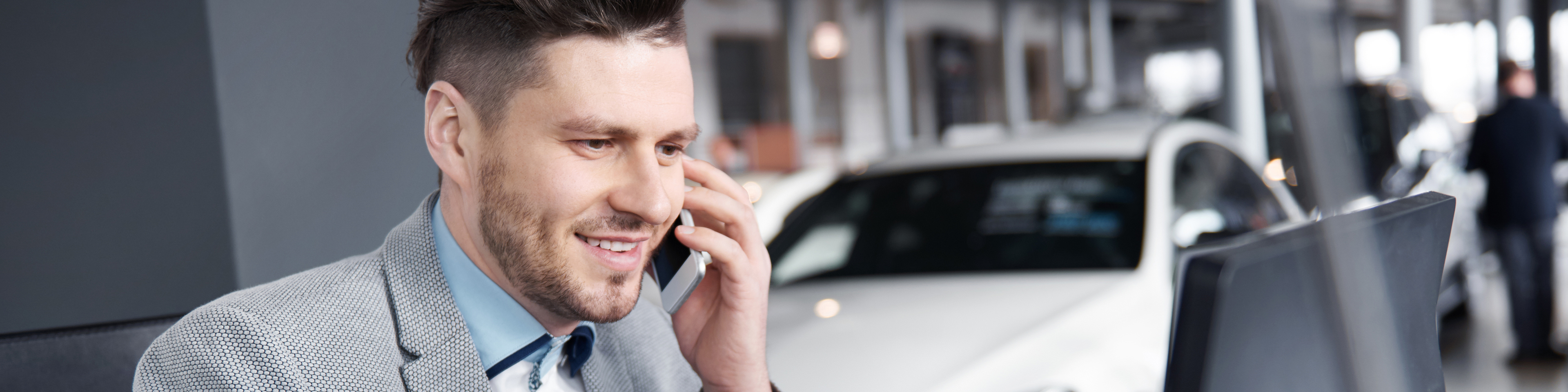 Man on phone and laptop at car dealership