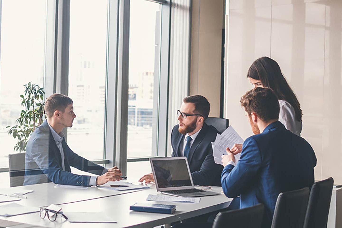 business people sitting around a desk in an office with a glass wall.