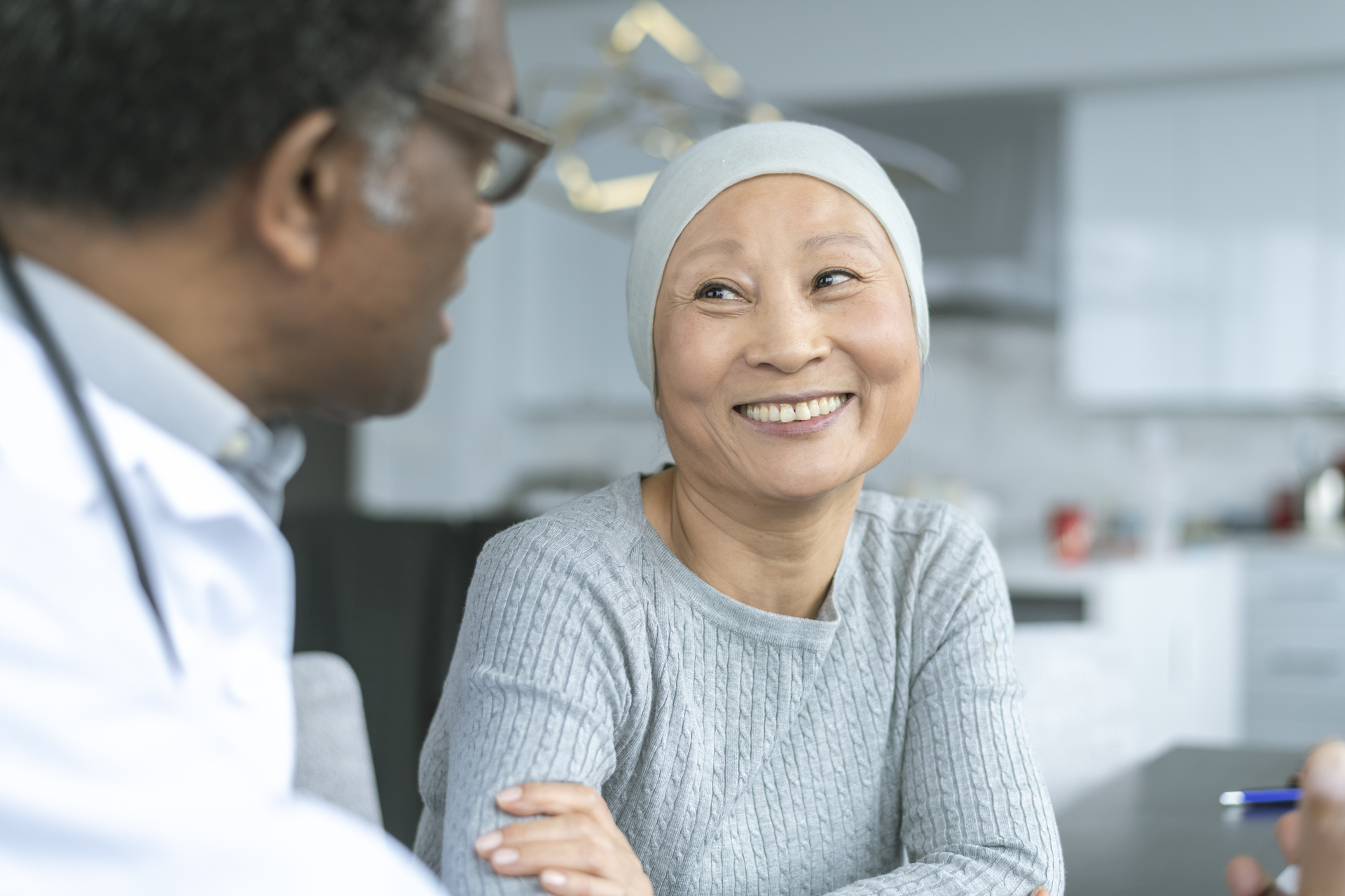 A Korean woman with cancer is meeting with her doctor. Chemotherapy treatment is going well. The patient is smiling at her doctor as he shares with her positive news.