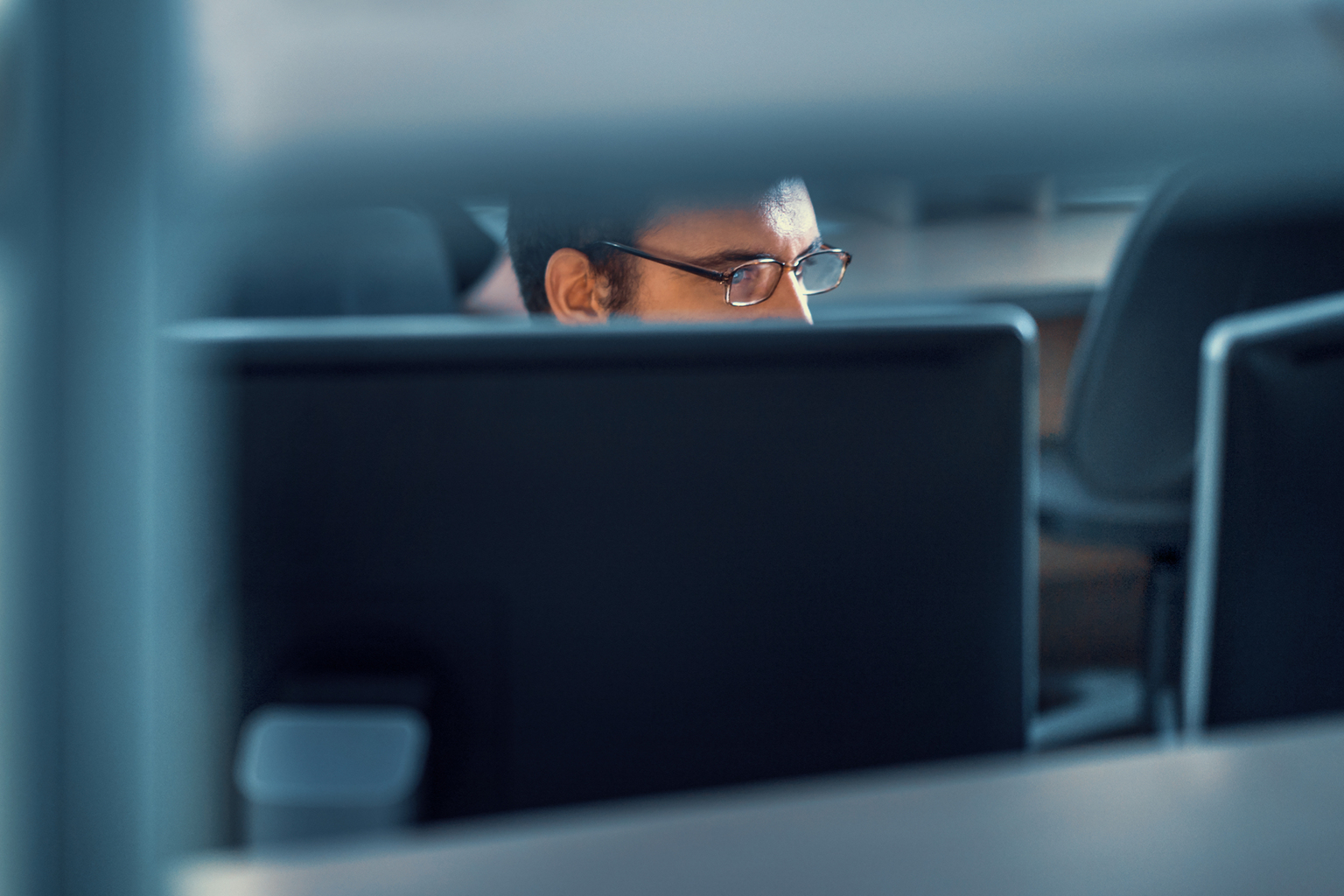 Closeup front view of deeply focus developer working on an application. He's sitting in front of dual display monitor, barely visible through office furniture