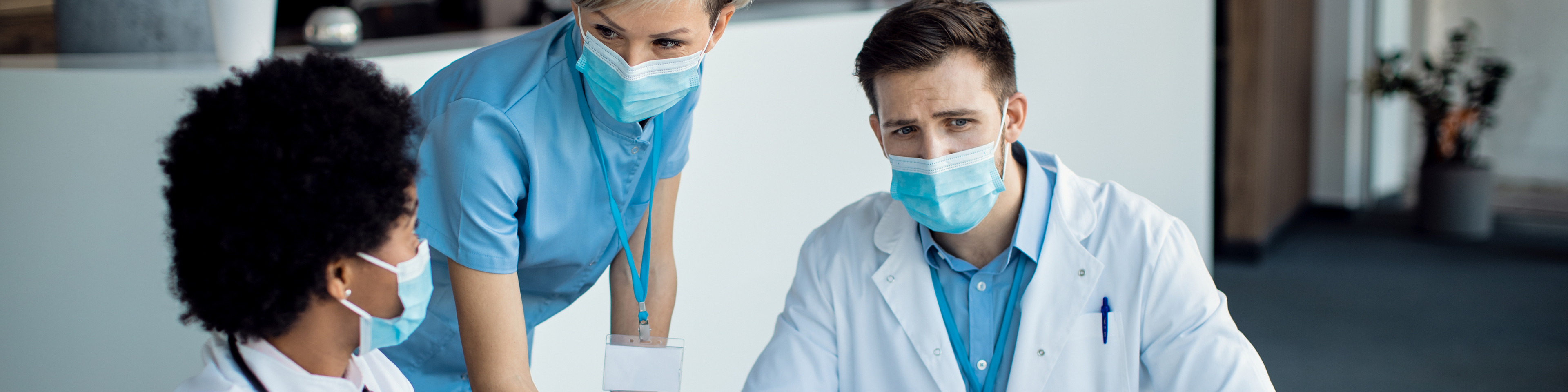 Group of mask wearing medical professionals talking while using laptop during a meeting in hospital