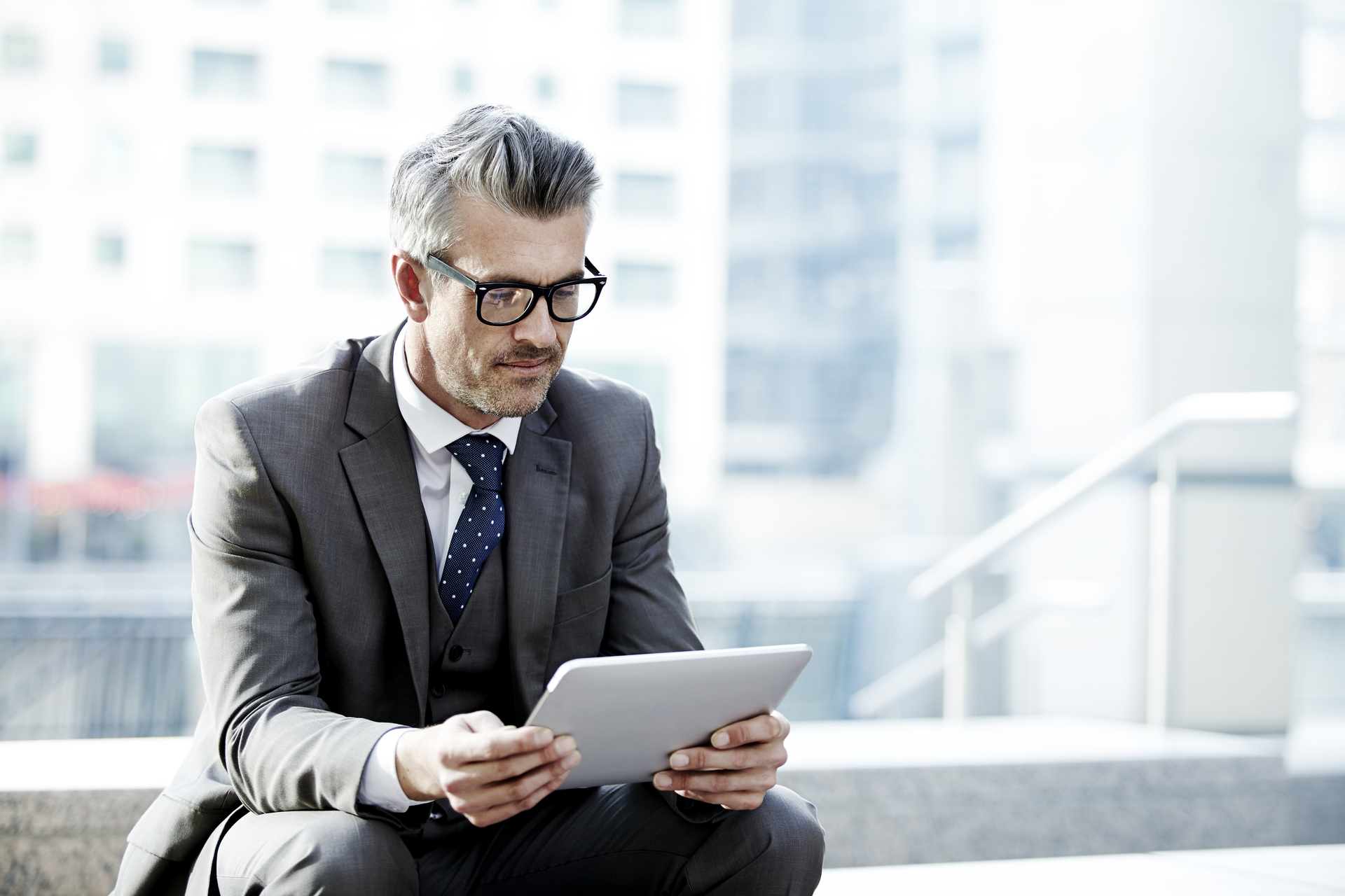 Man sitting outside office building, glancing, looking at tablet, grey, gray suit with polka dot tie, white dress shirt, Q3 2021, TAA NA US - Preparer