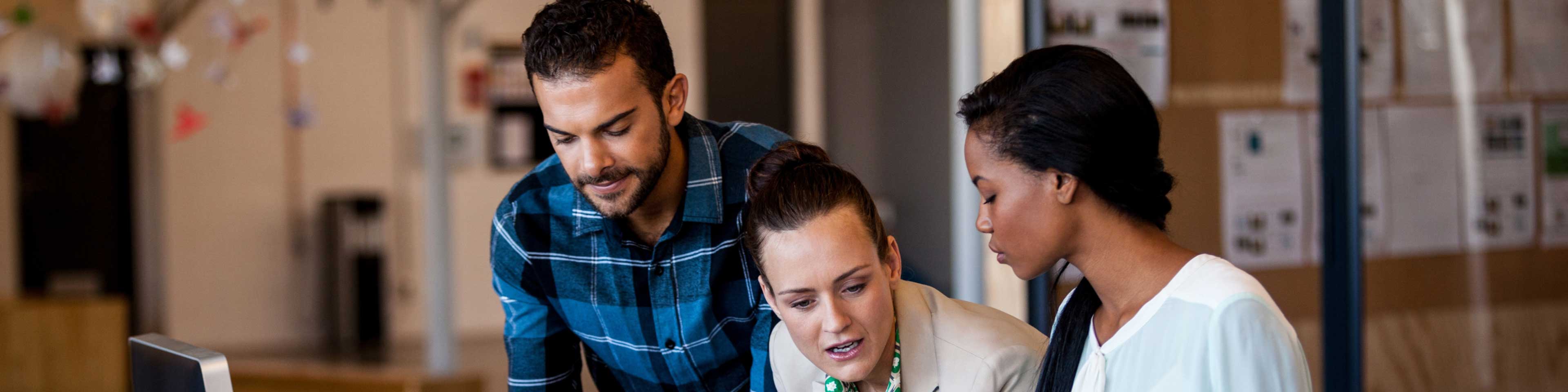 Three people standing at a desk discussing something 