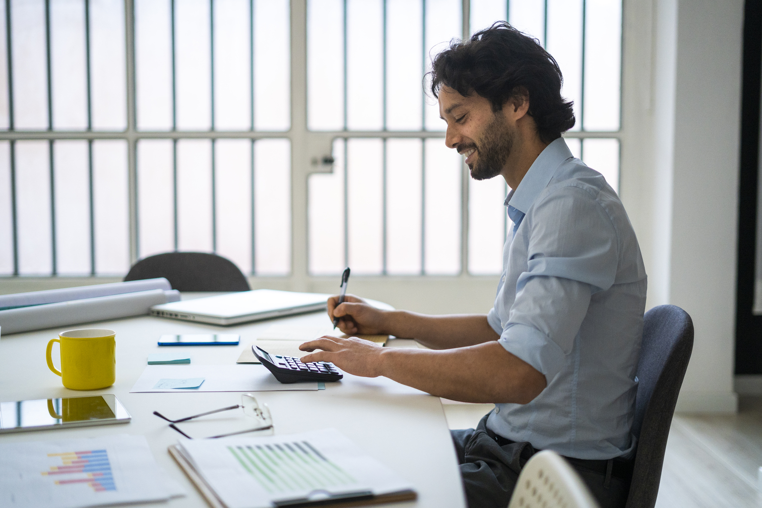 Smiling young businessman working while sitting by desk in office