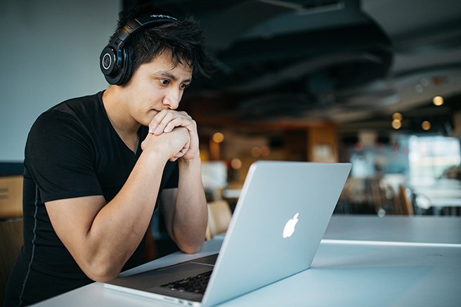 Man intently watching laptop screen with over ear headphones on