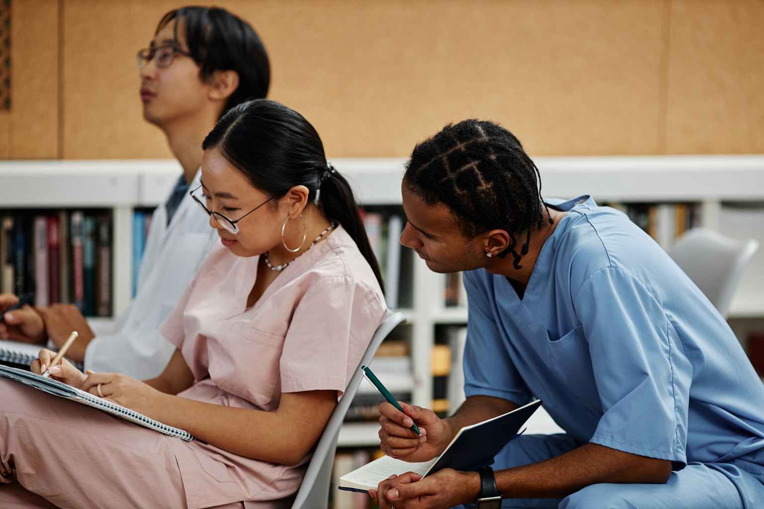 Two nursings students wearing pink and blue scrubs work together on classroom assignment