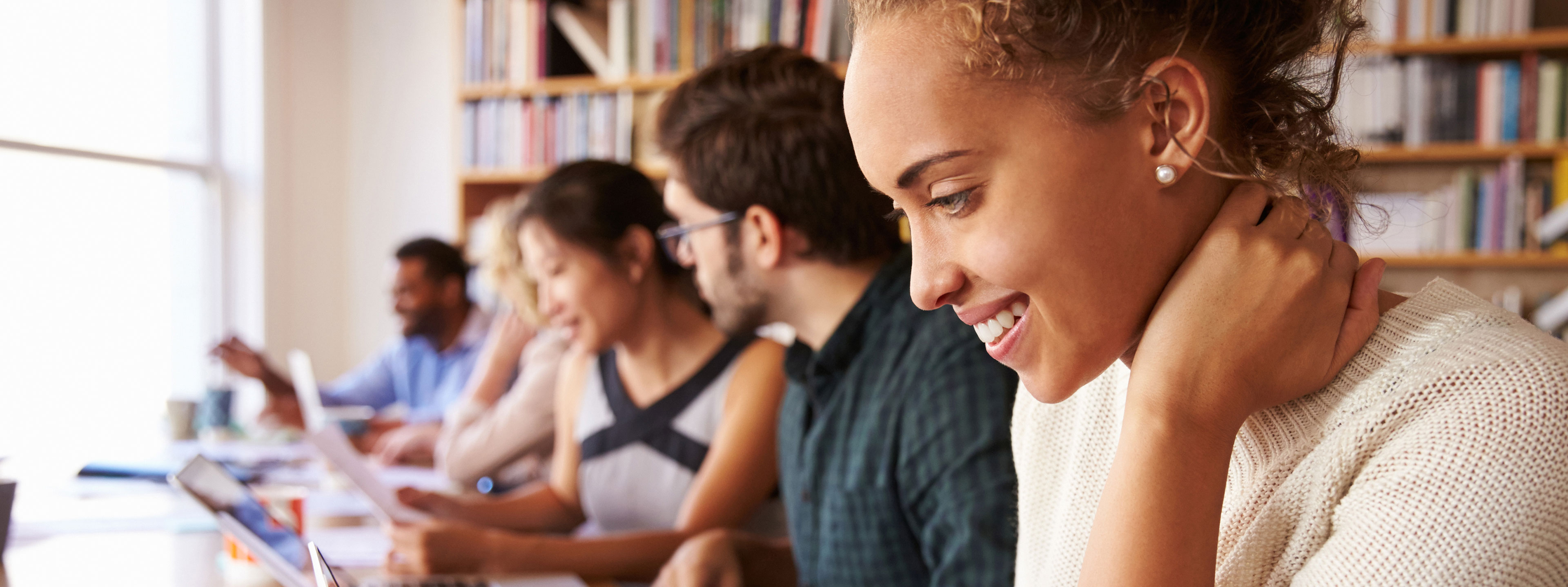 Multiple professionals in a library space reading print materials and using TeamMate on their computers.