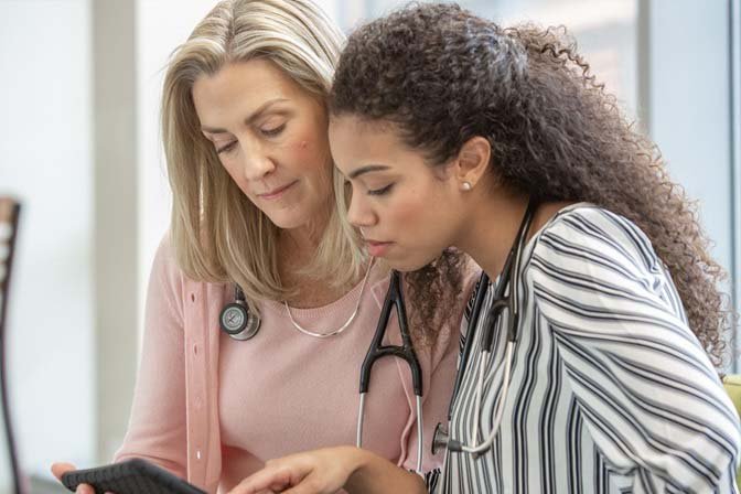 two females with stethoscopes pointing at a tablet