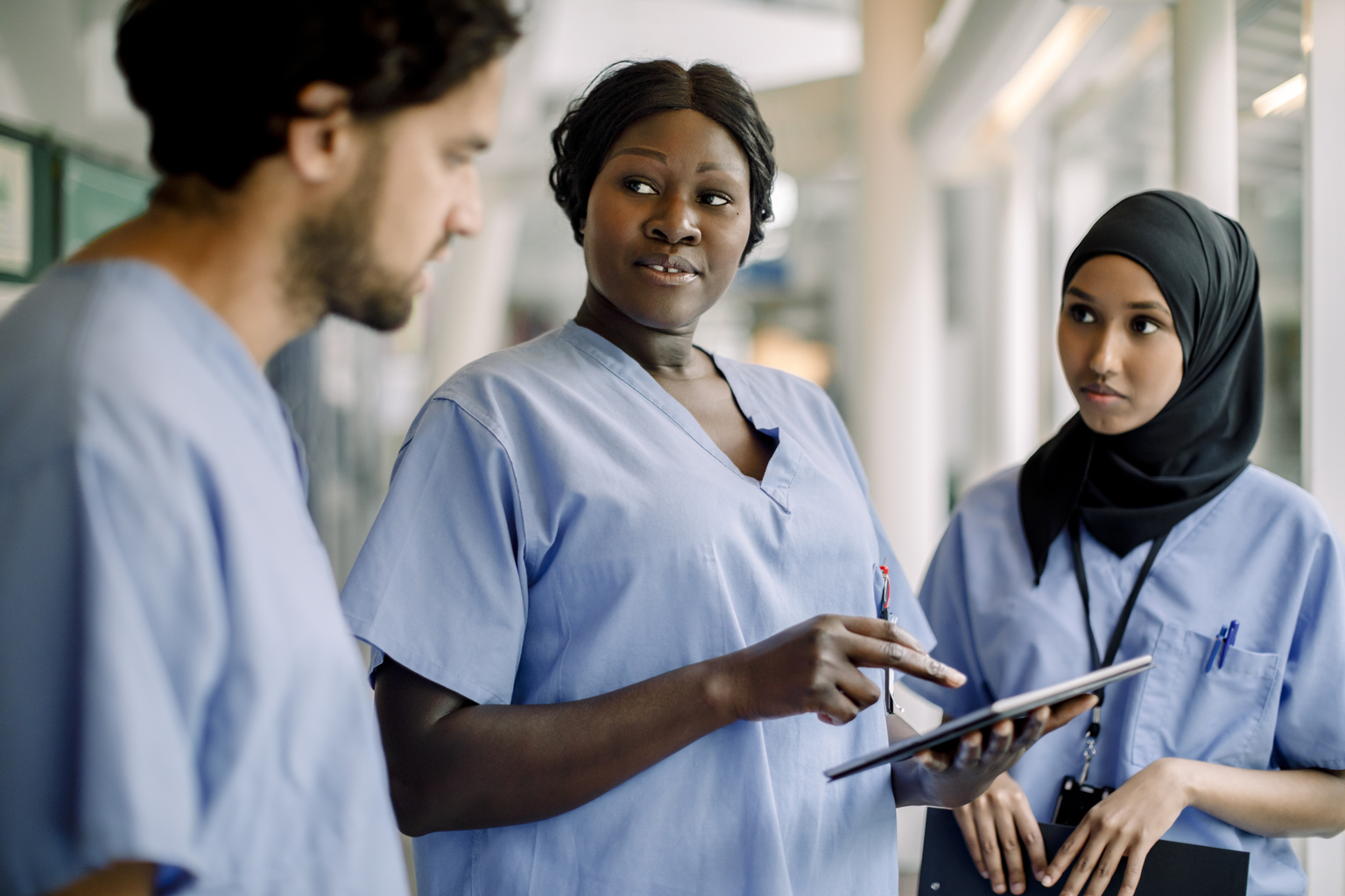 Female African nurse with digital tablet talking to colleagues in hospital.