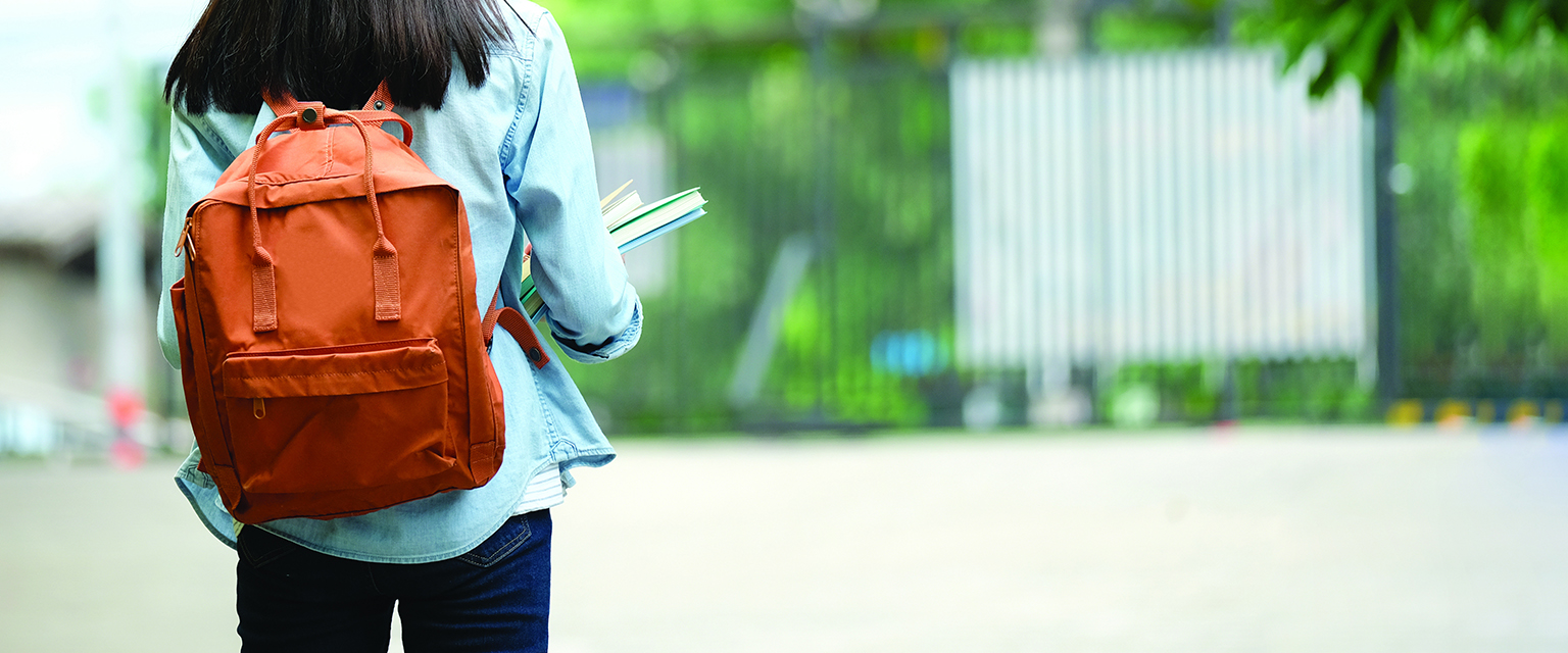 Back of student girl holding books and carry school bag while walking in school campus