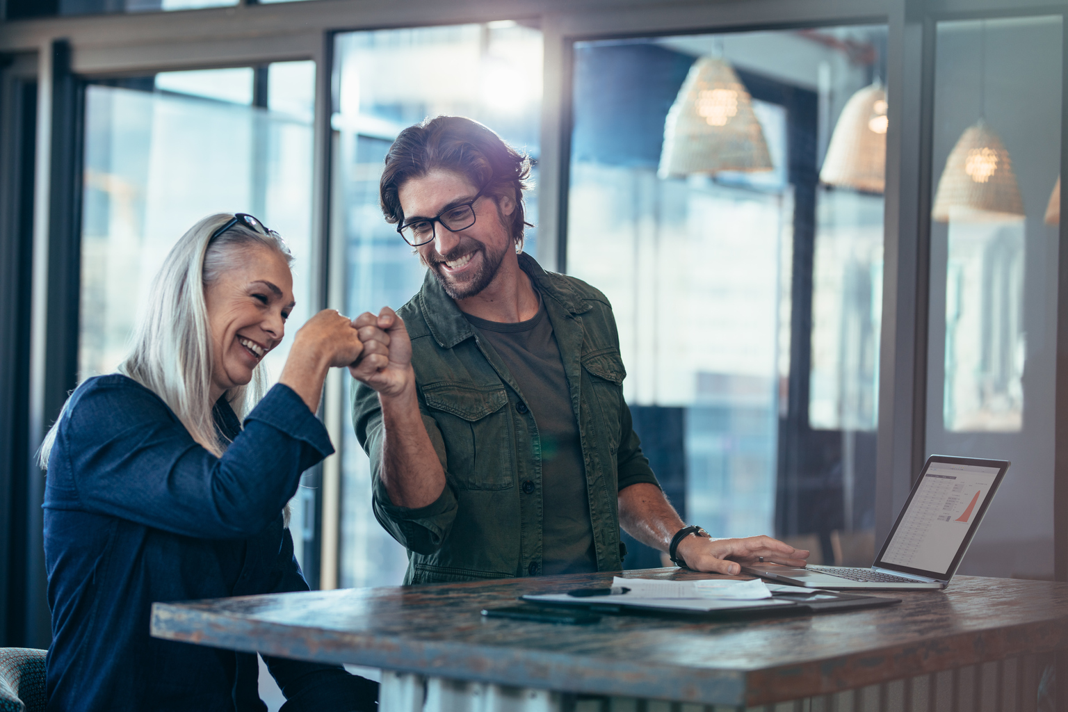 Young businessman and senior businesswoman making a fist bump at office. Business colleagues looking happy and excited after completion of project.