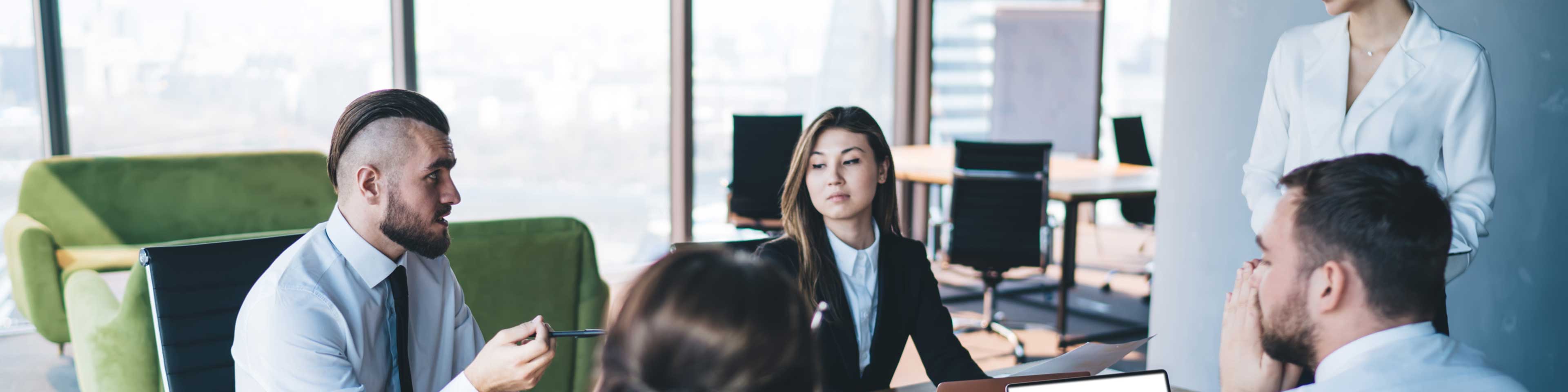 4 people sitting around a desk with one person standing as they discuss things