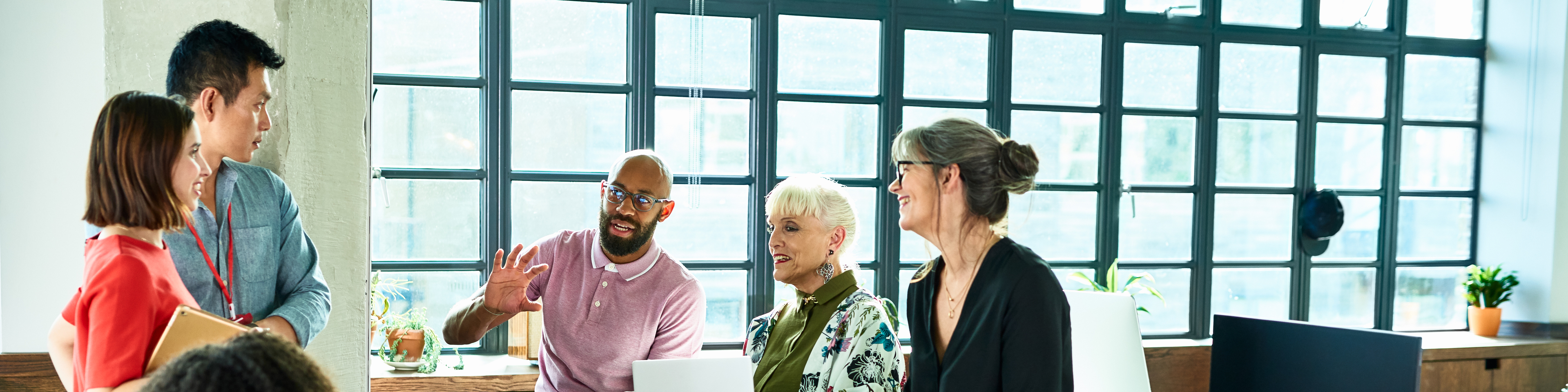 Diver group of mixed age and multi ethnic colleagues in discussion, mid adult man explaining and gesturing, woman with artificial limb smiling and listening