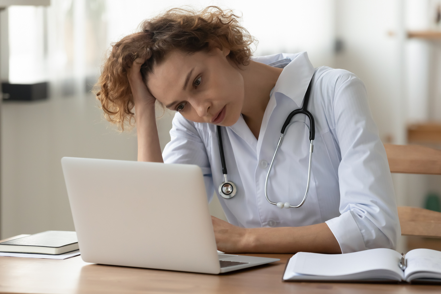Stressed young female doctor looking at laptop worried