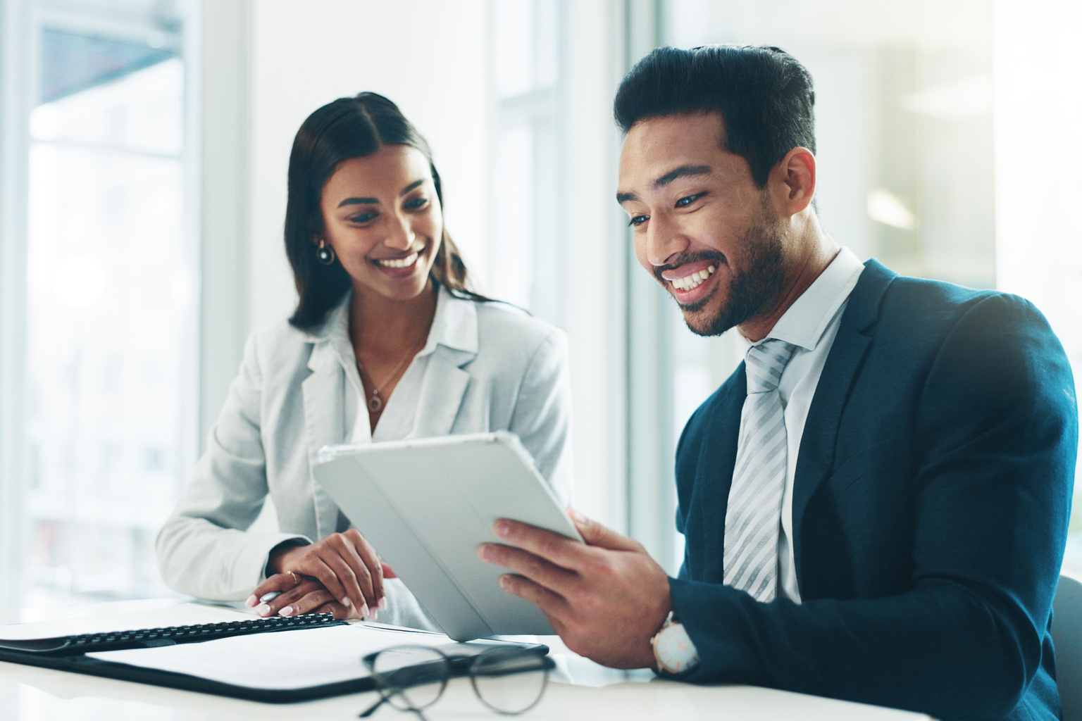 Two business colleagues sit together at conference table smiling at analysis results on tablet. 