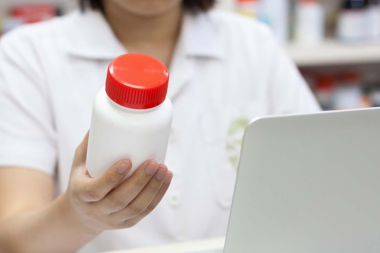 phamacist holding bottle of pills while using computer