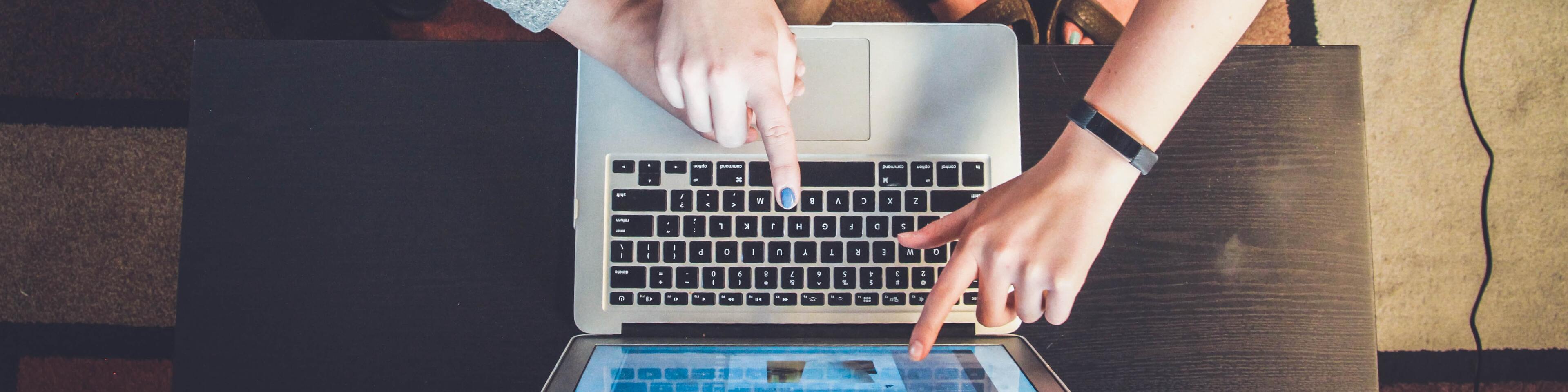 Three people pointing at the silver laptop computer