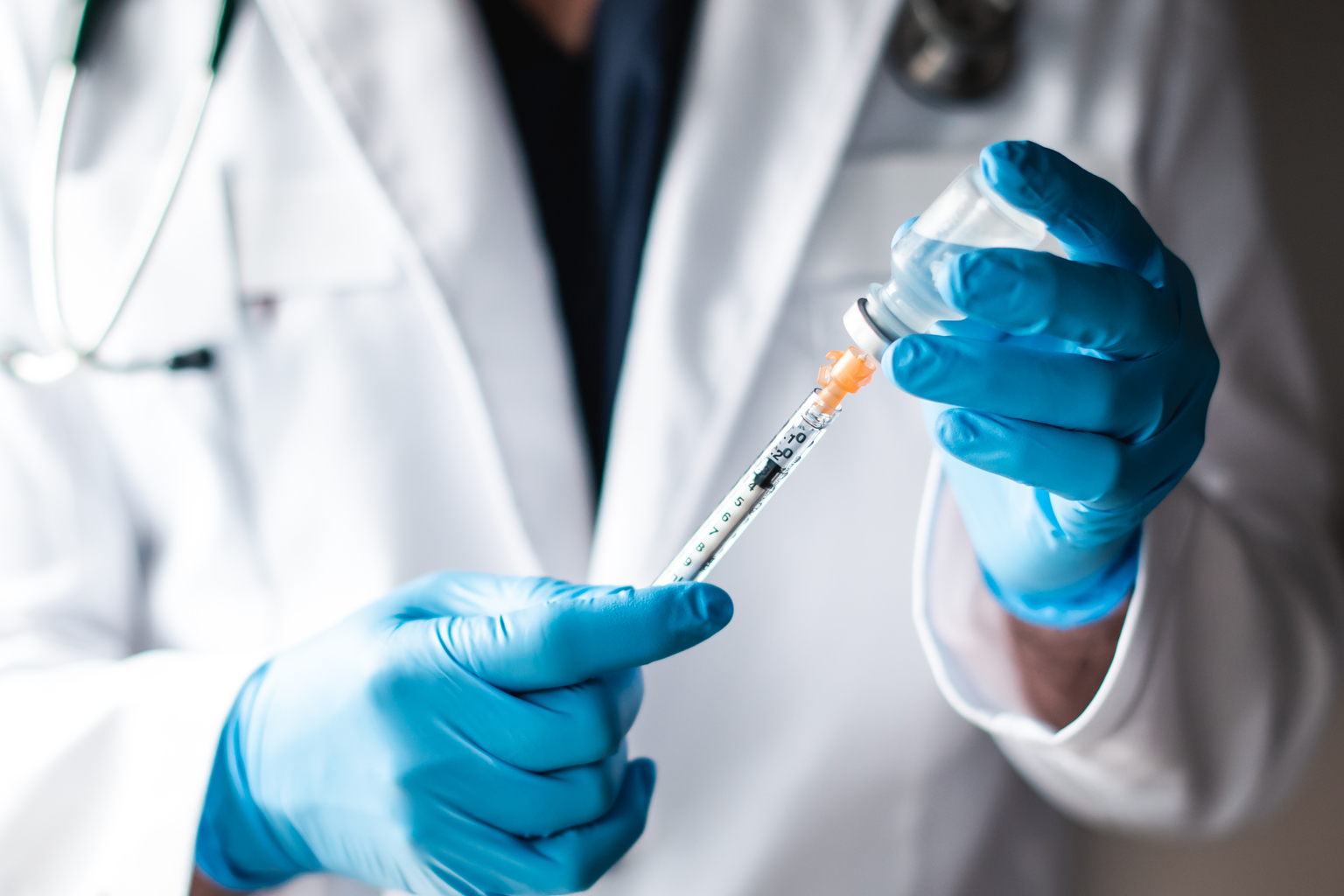 Doctor in white coat drawing vaccine into a syringe for injection.