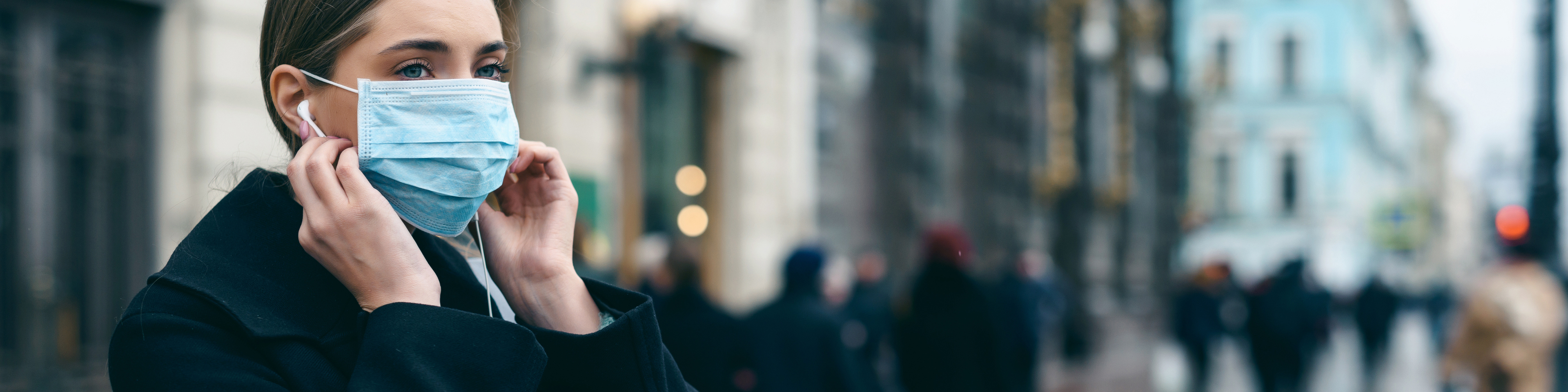 Woman outside on busy city sidewalk wearing a mask