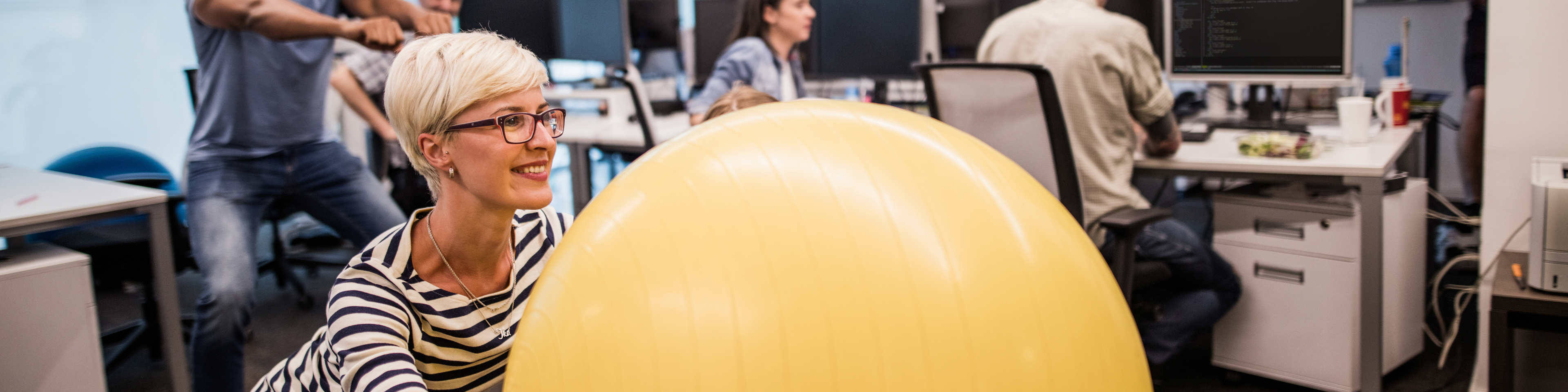 Happy female programmer exercising with fitness ball in the office