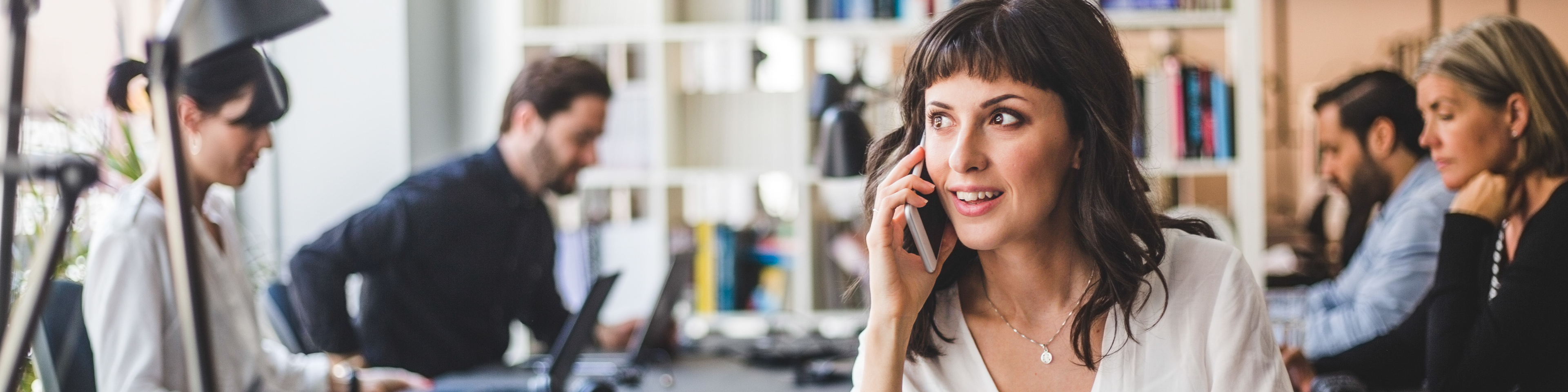 Businesswoman looking away while talking on mobile phone at desk in creative office