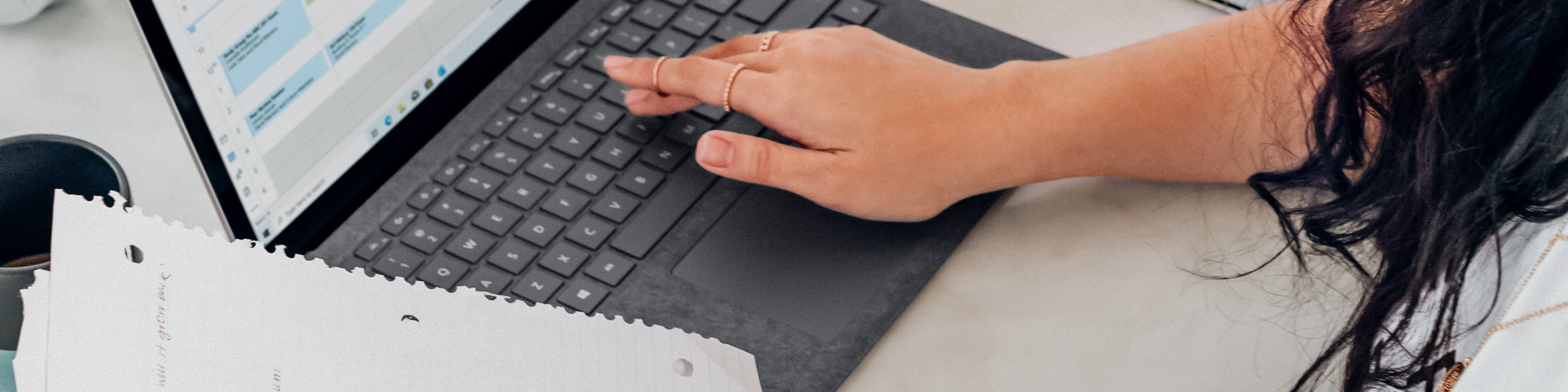 Woman holding papers in one hand and working at laptop keyboard with other