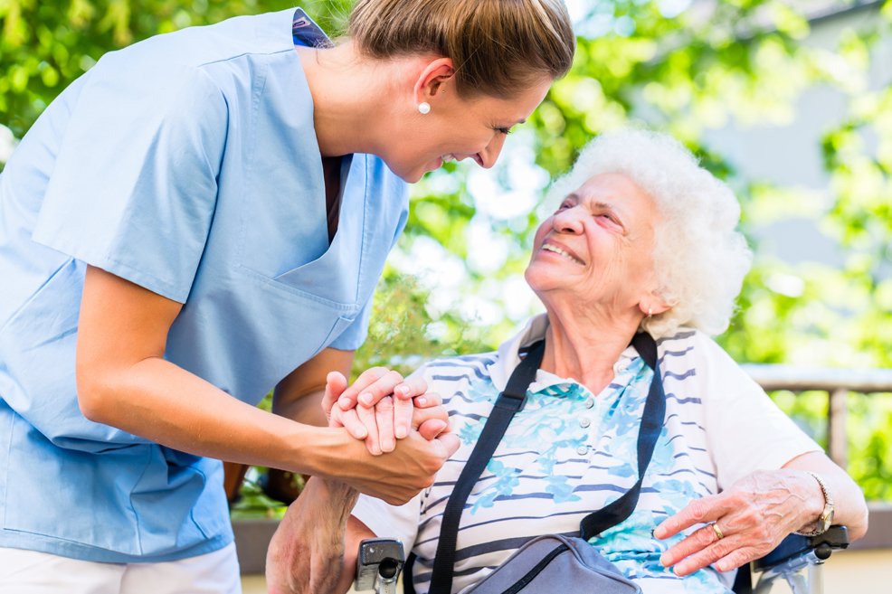 Nurse leaning down to and holding hand of older woman sitting in chair