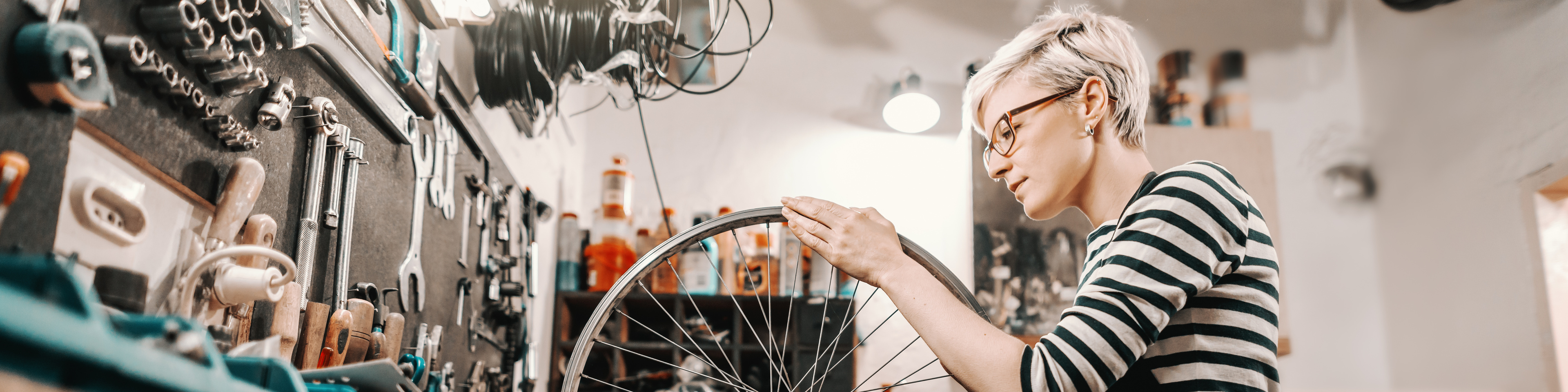 Female worker holding and repairing bicycle wheel while standing in bicycle workshop
