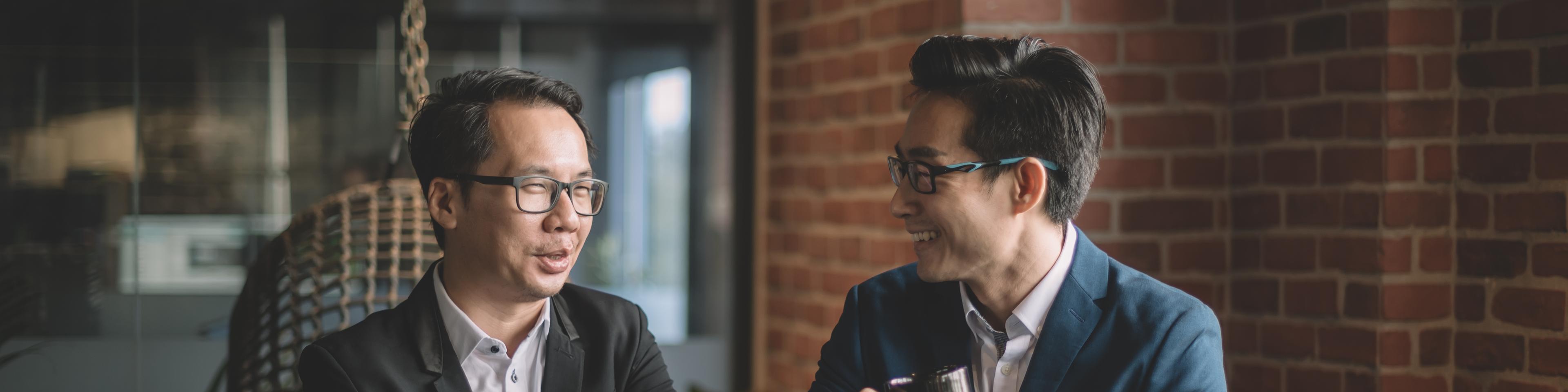 2 asian chinese white collar workers having discussion during their coffee break in lounge using laptop and digital tablet