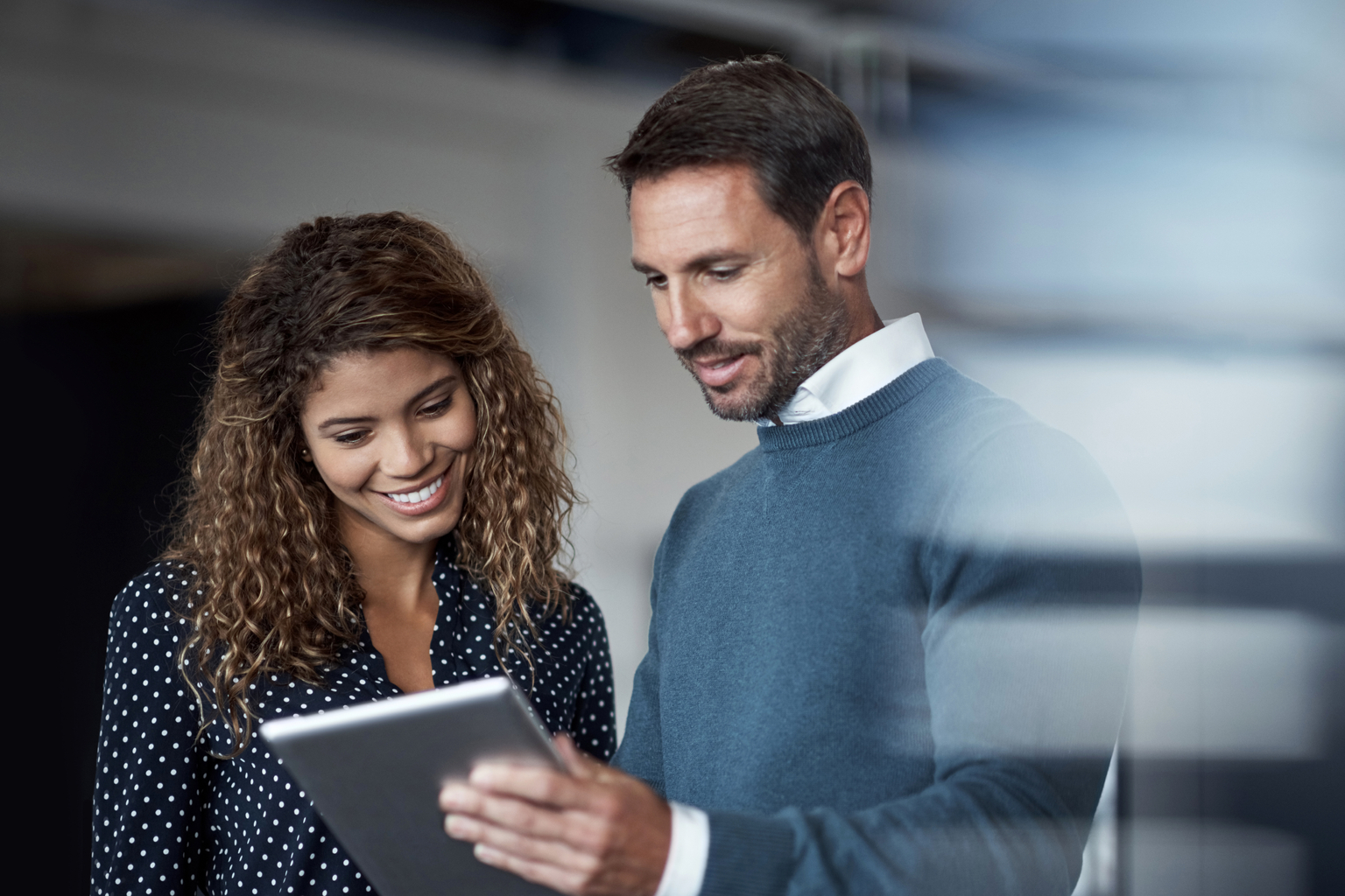 Shot of two colleagues working on a digital tablet together while standing in a large office