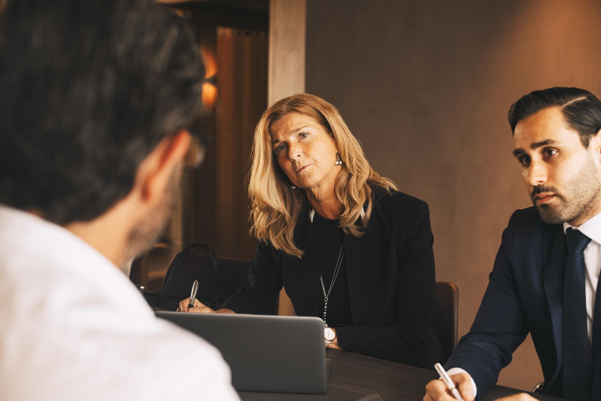 Serious legal coworkers listening to mature businessman during meeting at law office