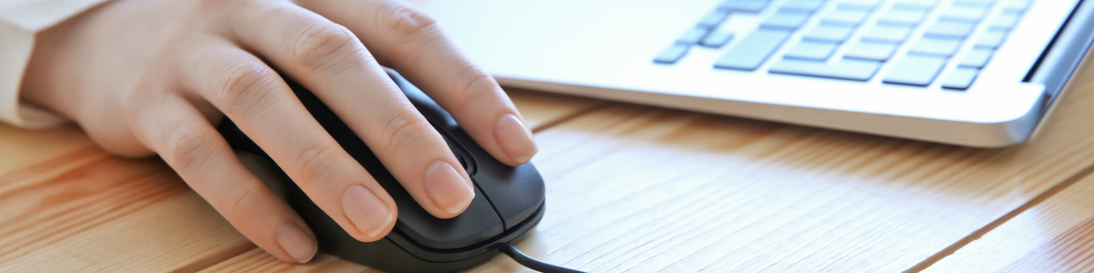 feminine hand sitting on top of a black computer mouse, macbook air keyboard in the background