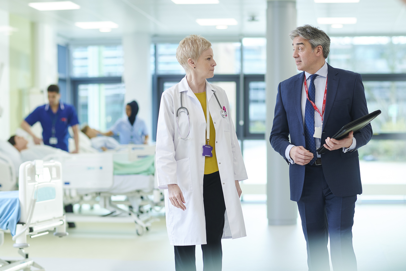 a women doctor with short blonde hair talking with a business man with navy suit in hospital