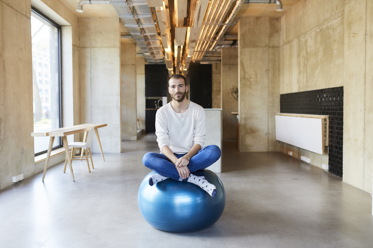 Portrait of young man sitting on fitness ball in modern office