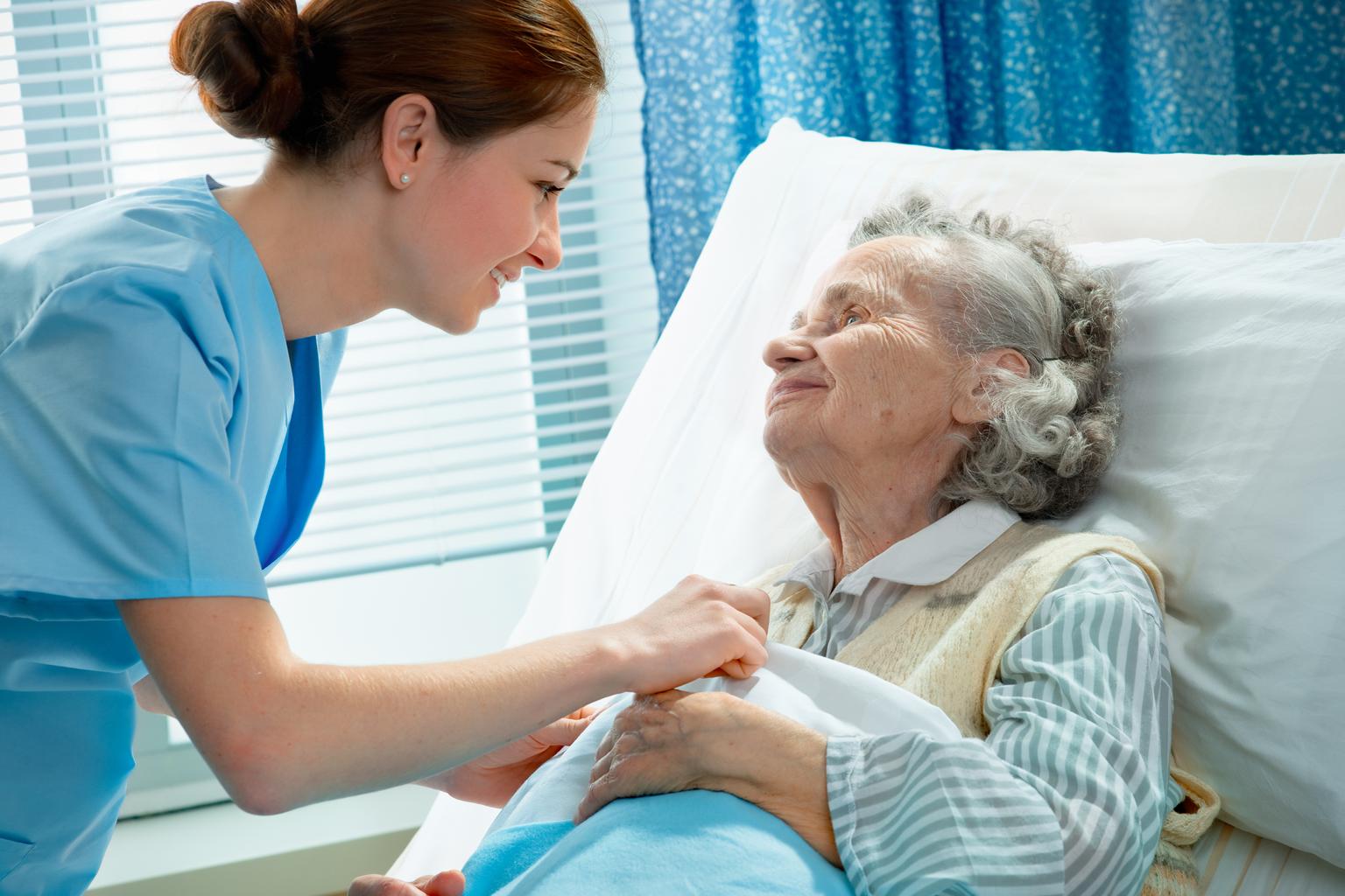 A nurse leans over patient bedside to take care of senior patient