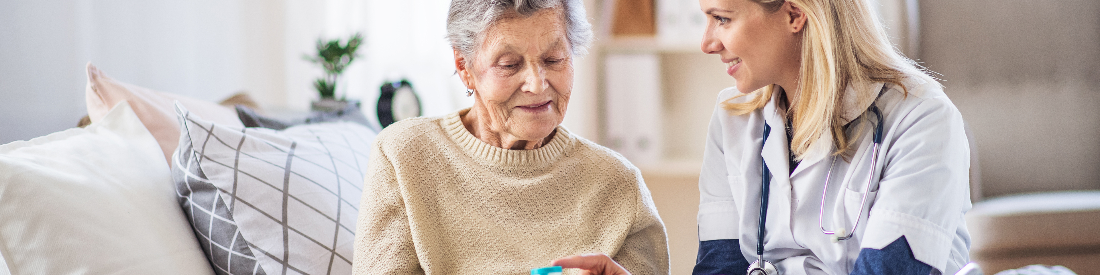 Home health nurse sitting with patient talking to her about the medication bottle patient is holding