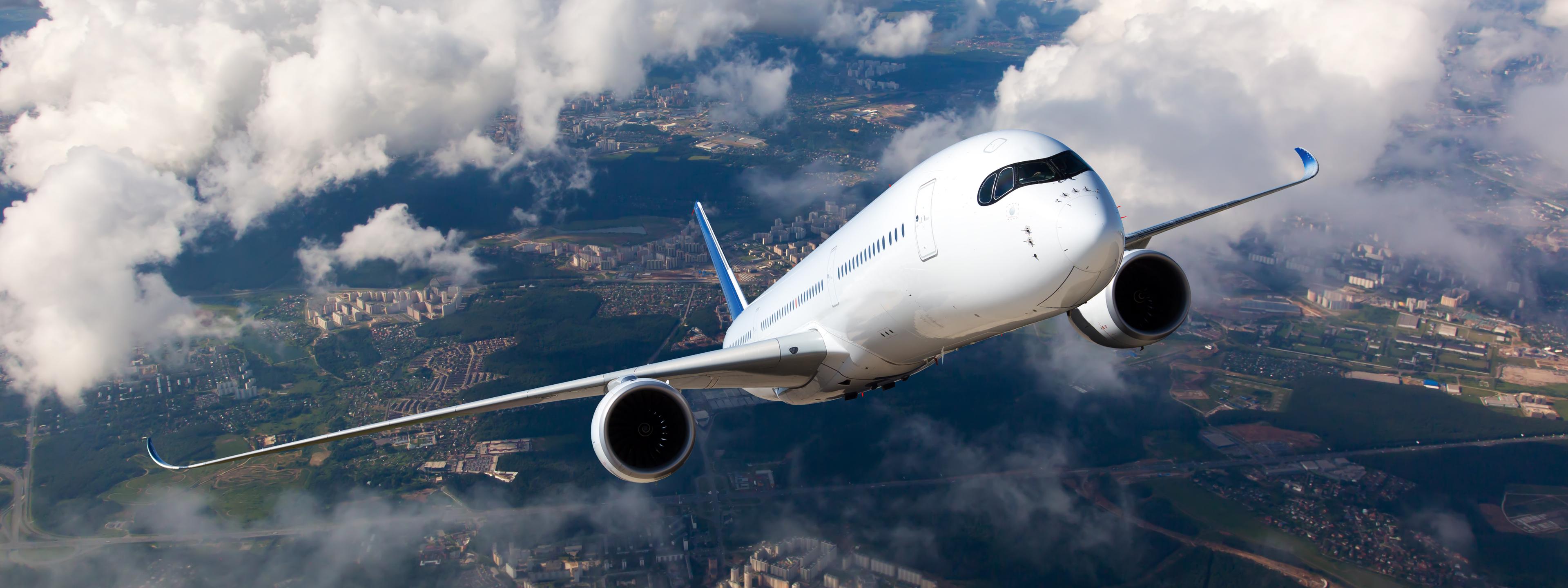 White passenger plane climbs through the clouds. Aircraft is flying high above the city.