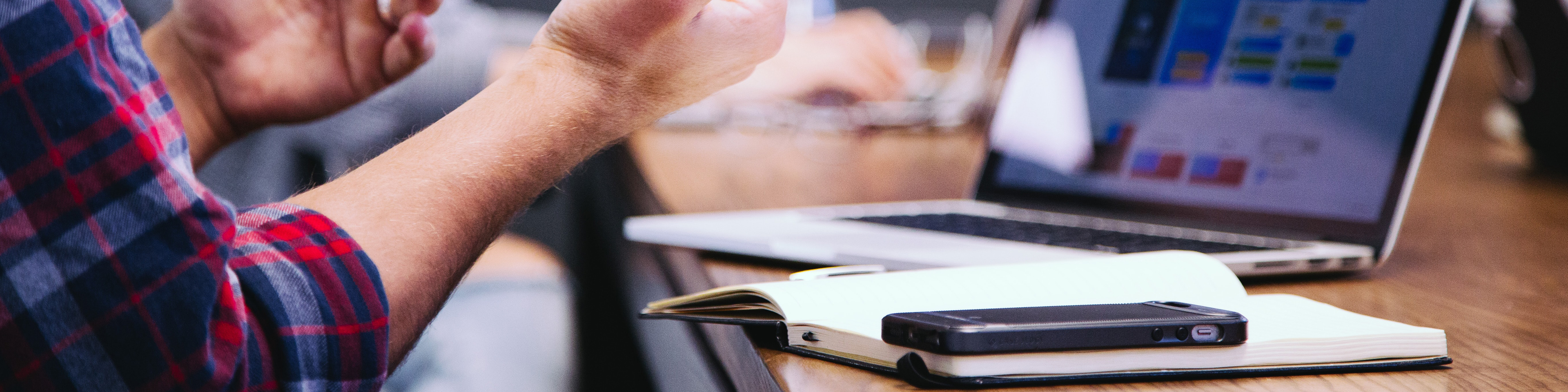 Close up on man sitting at laptop, notepad and phone on desk, gesturing with hands