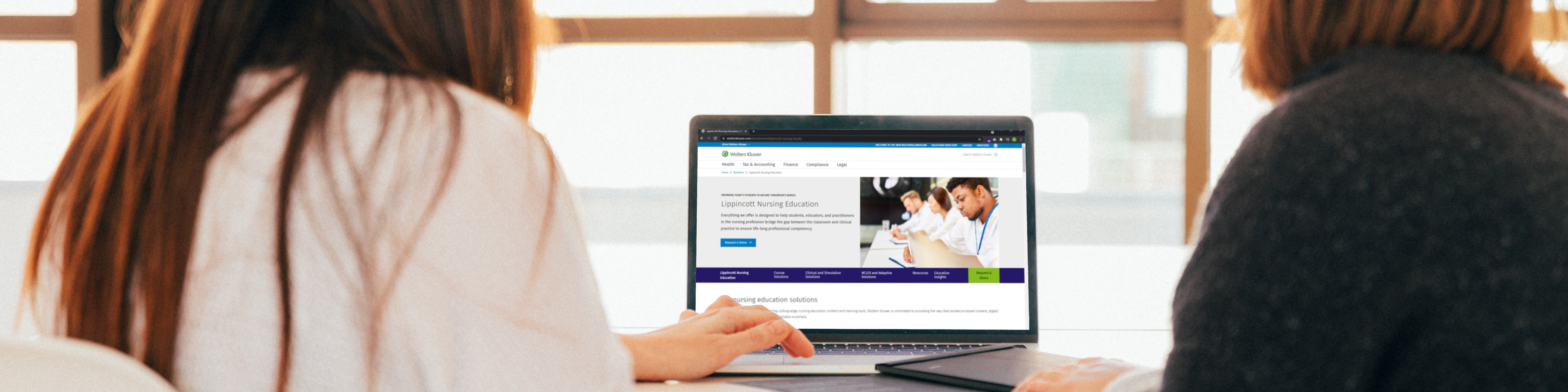 Two women looking at Lippincott Nursing Education website on a laptop screen, their backs to the camera