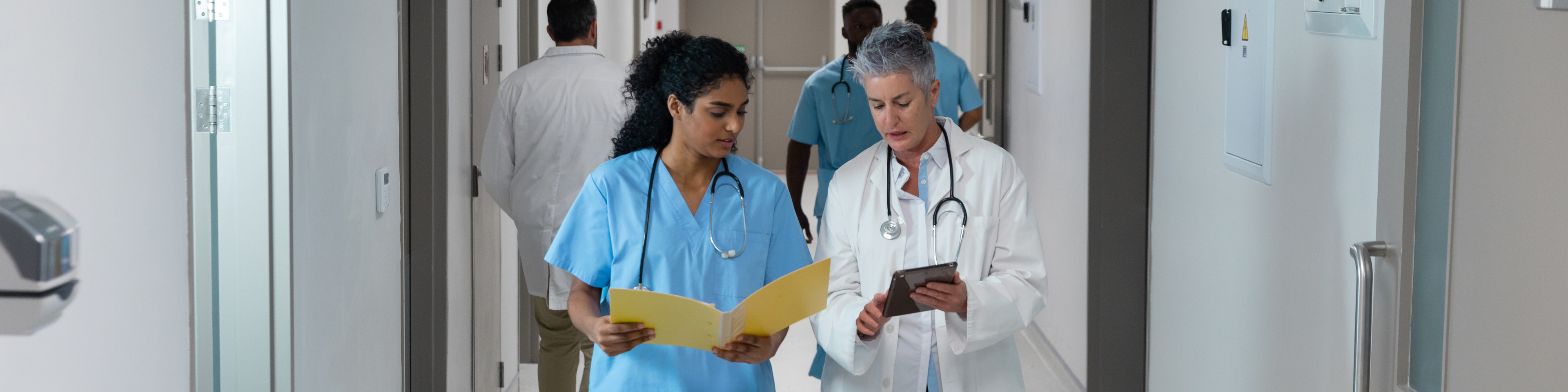 Diverse male and female doctors walking through hospital corridor discussing