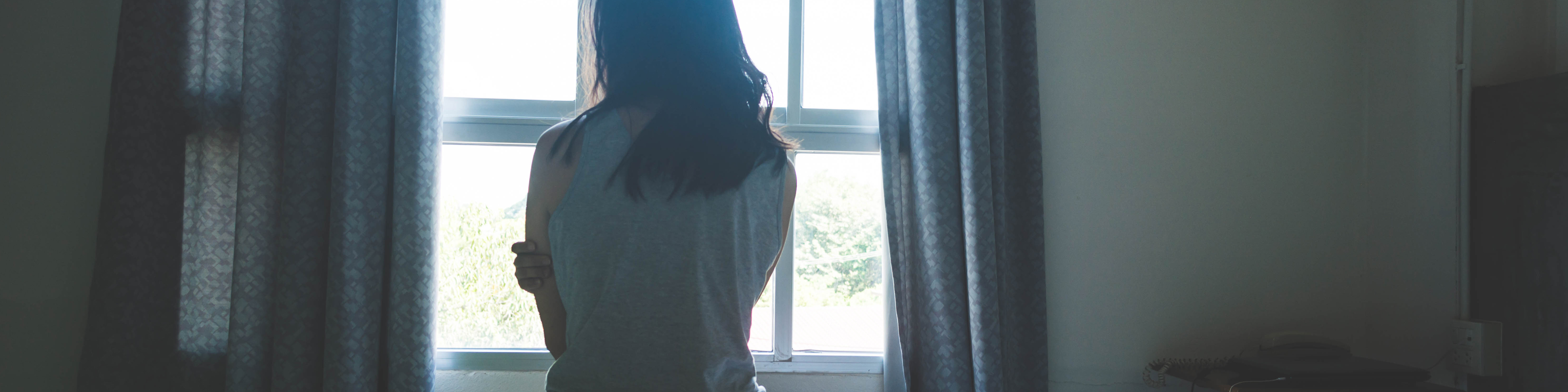 Woman sitting on bed in room with light from window