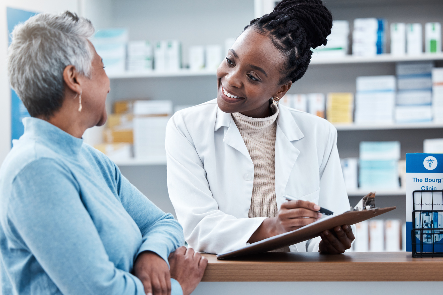 Pharmacist holding a clipboard, talking with a customer at the pharmacy desk