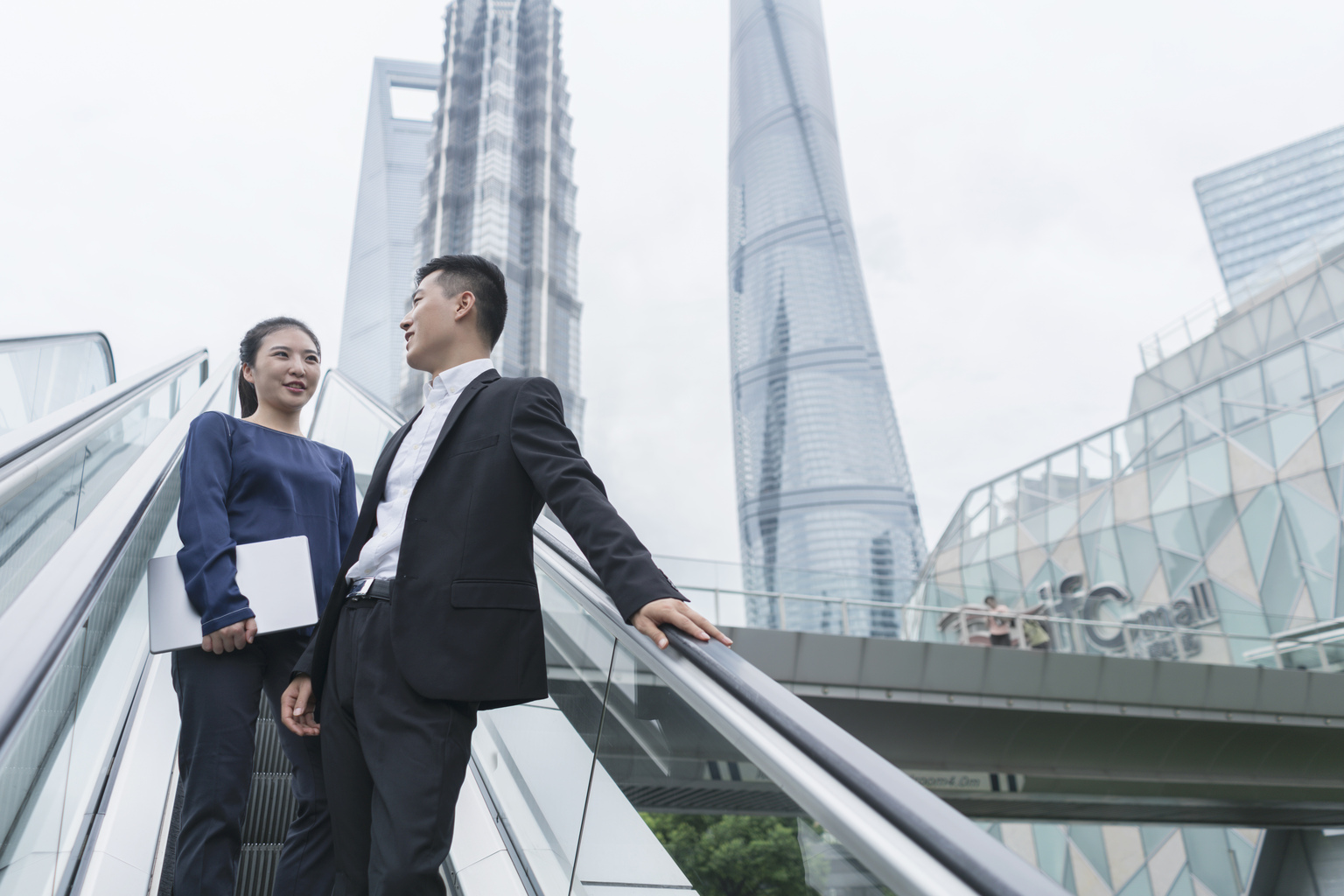 Young businesswoman and man talking while moving up city escalator, Shanghai, China