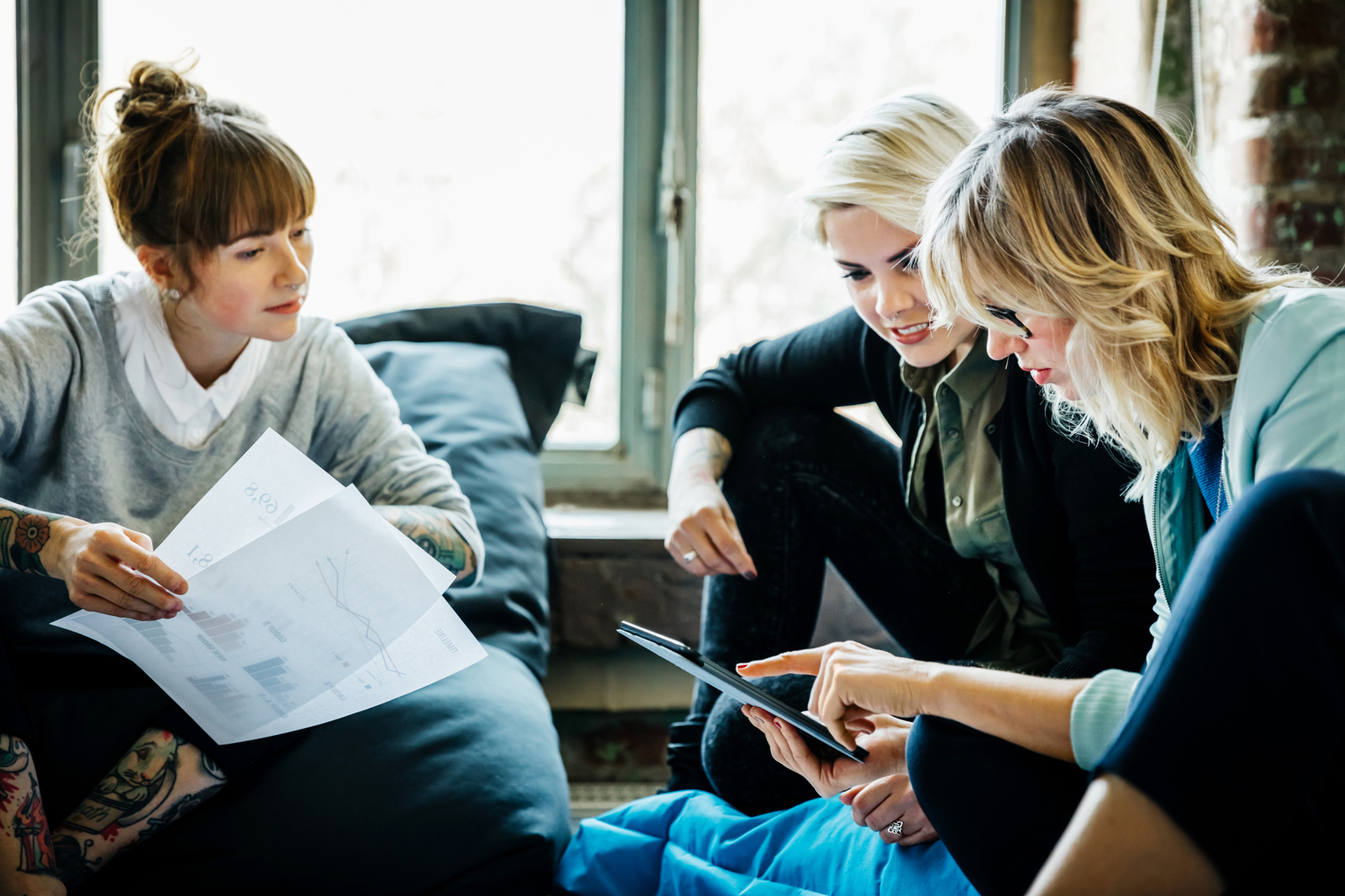 Professional women sitting casually on the floor discussing data on sheets and devices