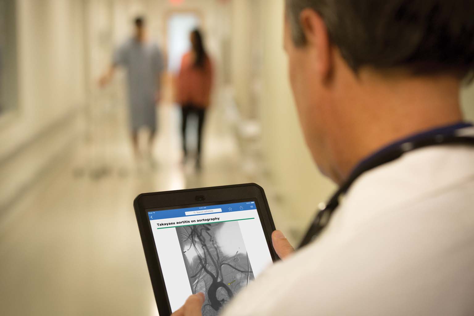 doctor paused in hallway looking at UpToDate on tablet